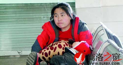 候車廳里，一位母親抱著睡著的孩子發(fā)呆